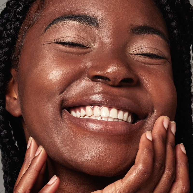 Smiling woman with glowing skin gently touching her face.