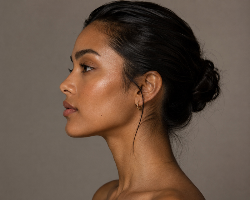 Side profile portrait of a woman with dark hair in a low bun against a neutral background.
