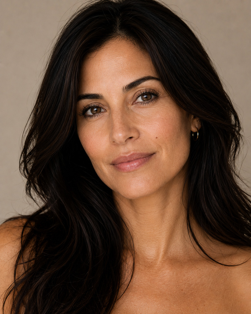 Close-up portrait of a woman with long dark hair looking toward the camera against a neutral background.